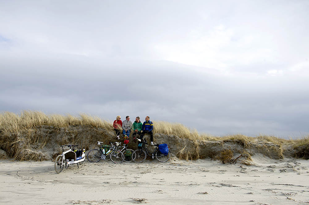 Four people sitting on a sanddune next to their bikes